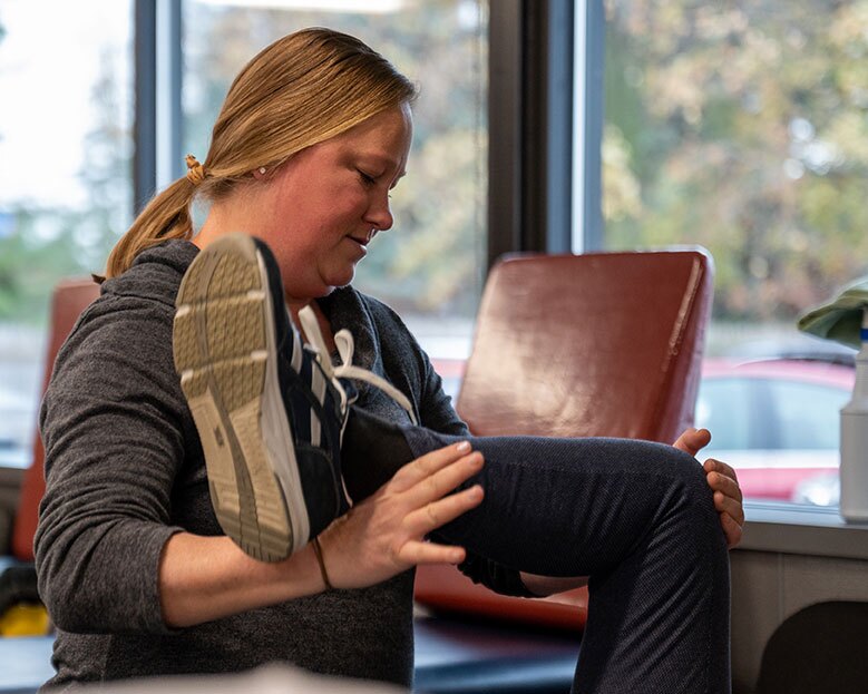 A physical therapist assistant smiles as she bends the leg of her patient.