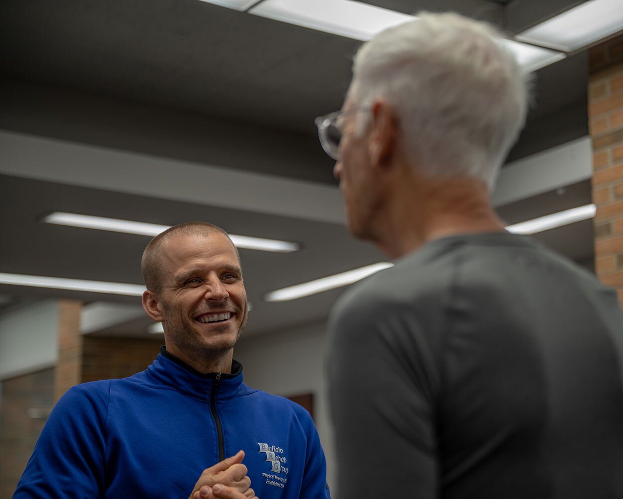 A physical therapist smiles as he converses with his patient.