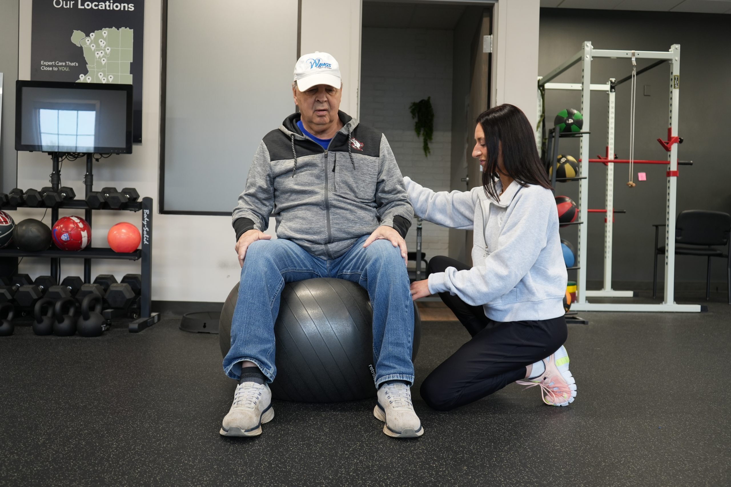 A physical therapist helps her patient balance on a yoga ball.