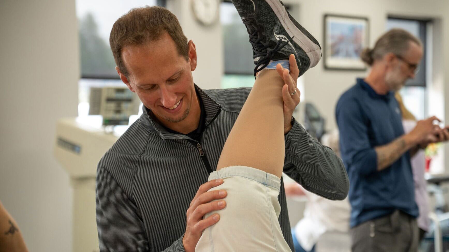 A physical therapist watches as his patient walks with a medicine ball.