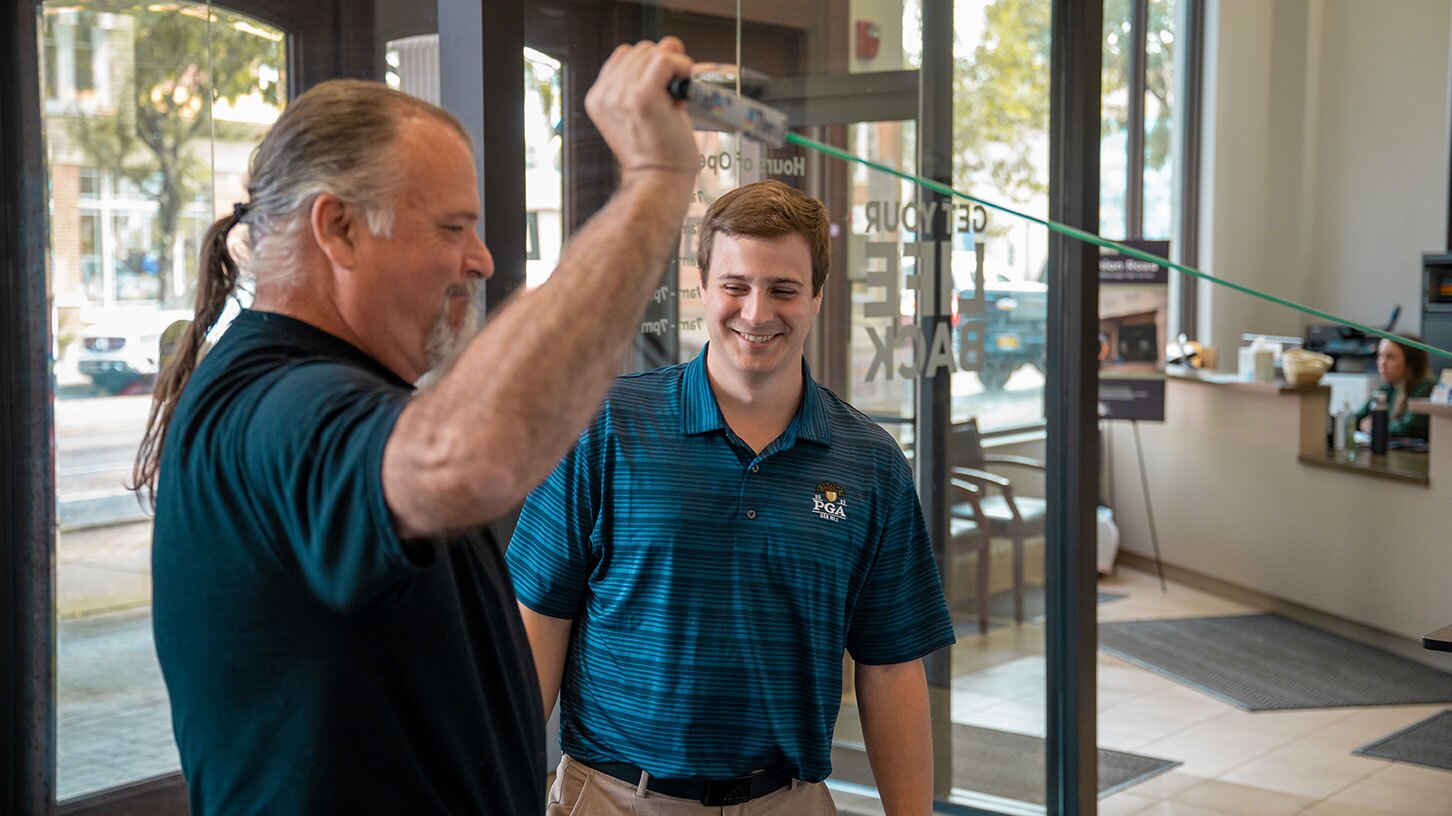 A physical therapist smiles as his patient stretches an arm over his head.
