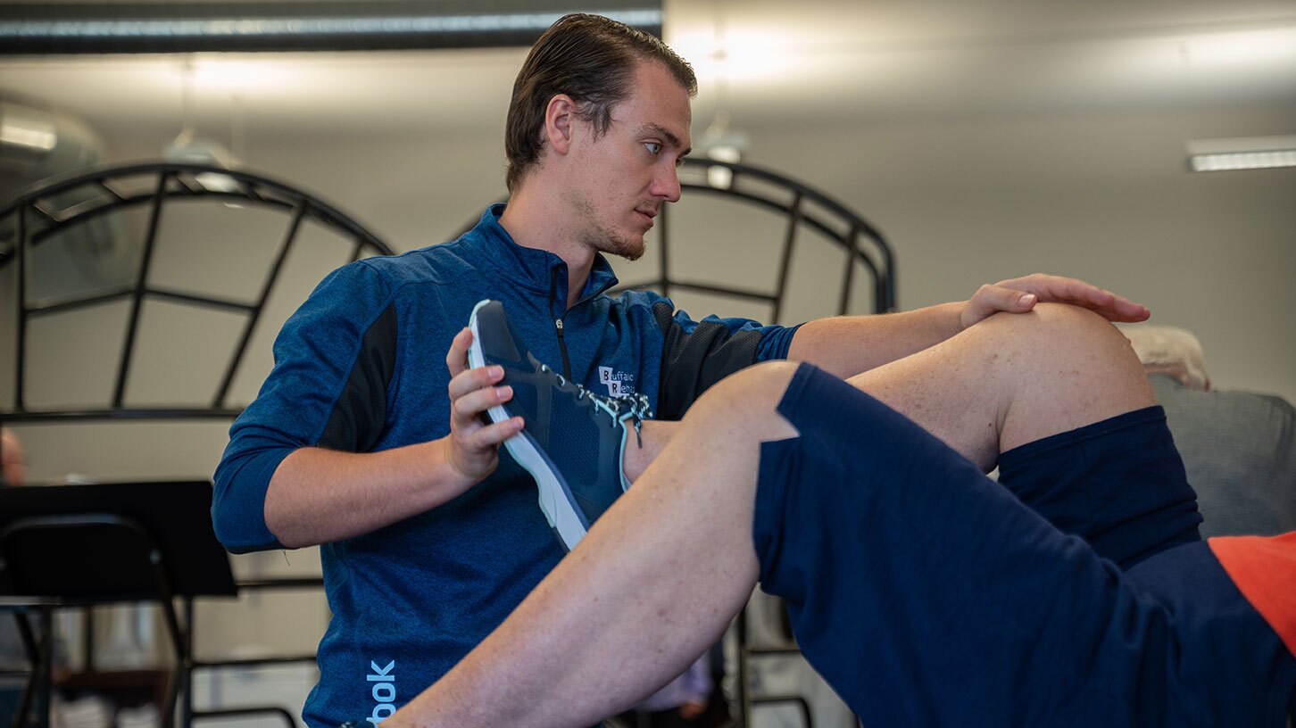 A physical therapist focuses as he stretches the knee of his patient.