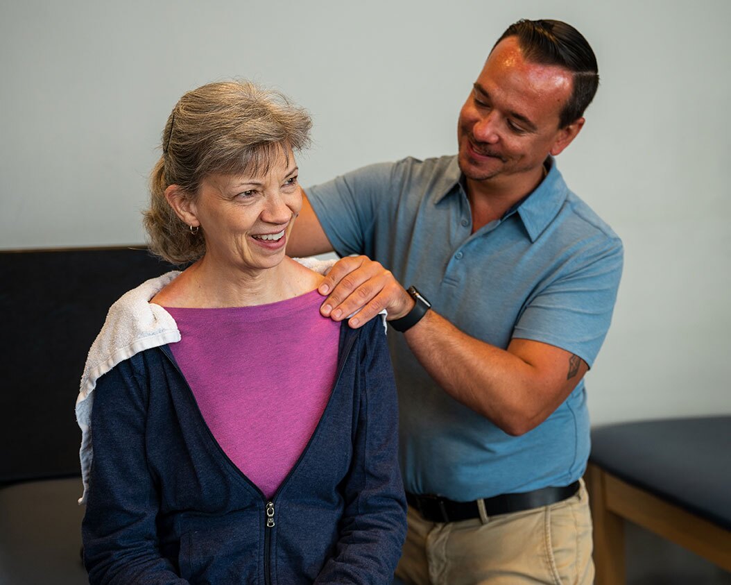 A man smiles as he massages the shoulders of his female patient.