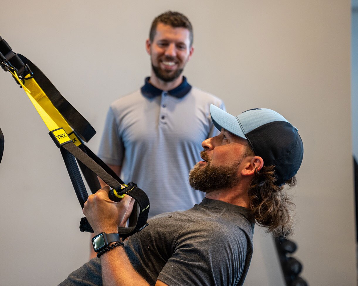 A physical therapist smiles as his patient pulls a resistance band.