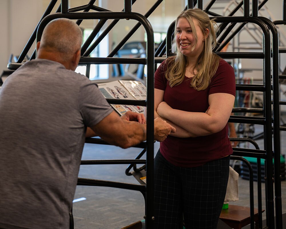 A physical therapy assistant smiles as her patient stretches his back.
