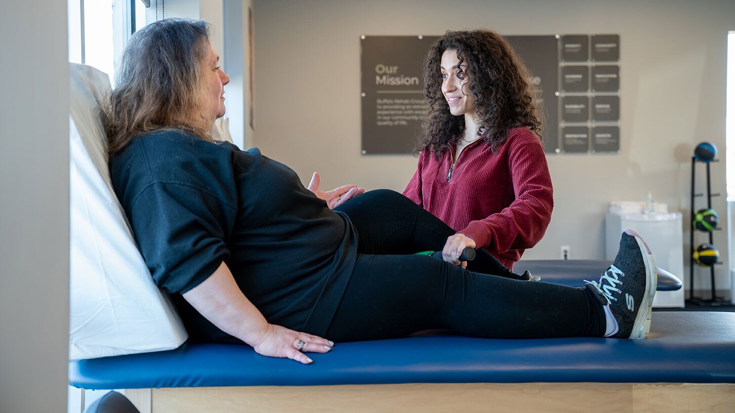A physical therapist assistant smiles as she talks to her patient.