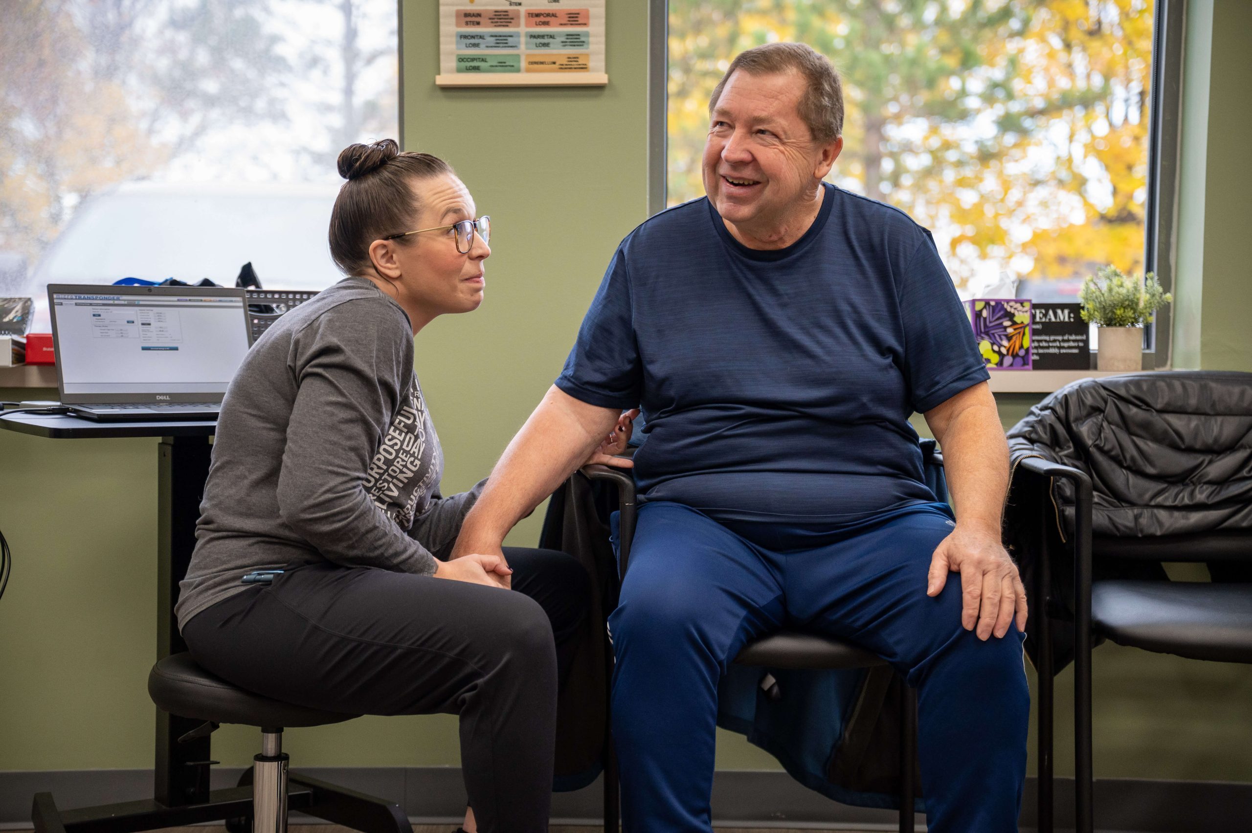 An image of a young, female occupational therapist working with an older gentleman in a clinic.