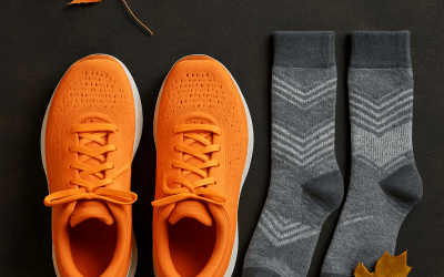 Flat lay of bright orange running shoes and gray socks with autumn leaves on a dark textured surface.